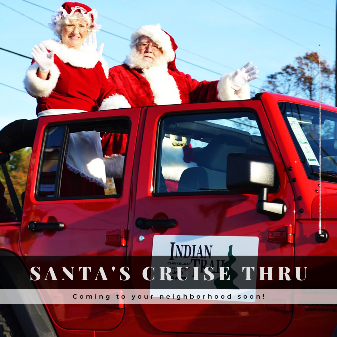 Santa and Mrs. Claus waving while riding in a red Jeep during a Christmas parade.