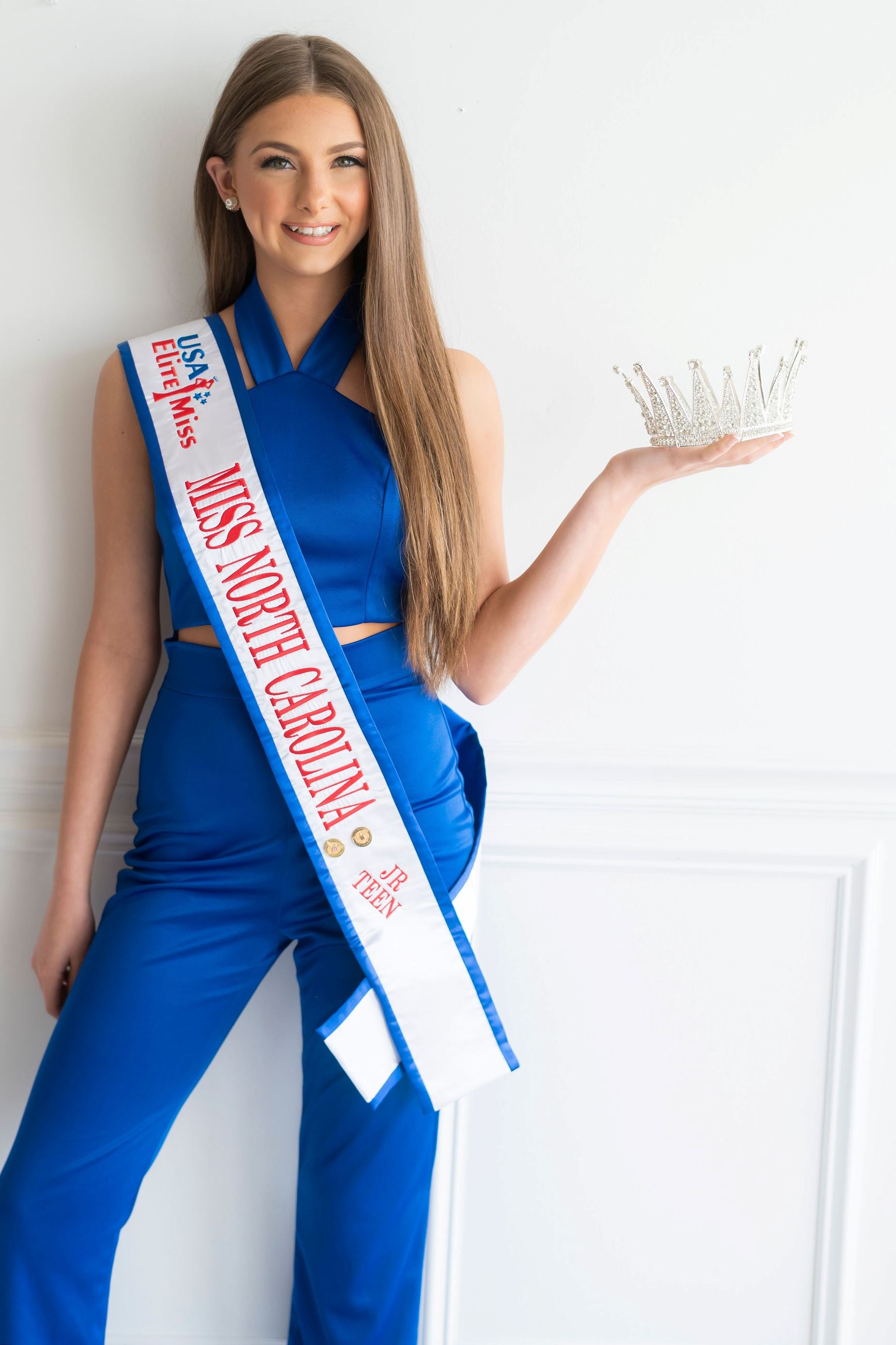Grace Laney, dressed in blue, holds a crown and wears a pageant sash. 