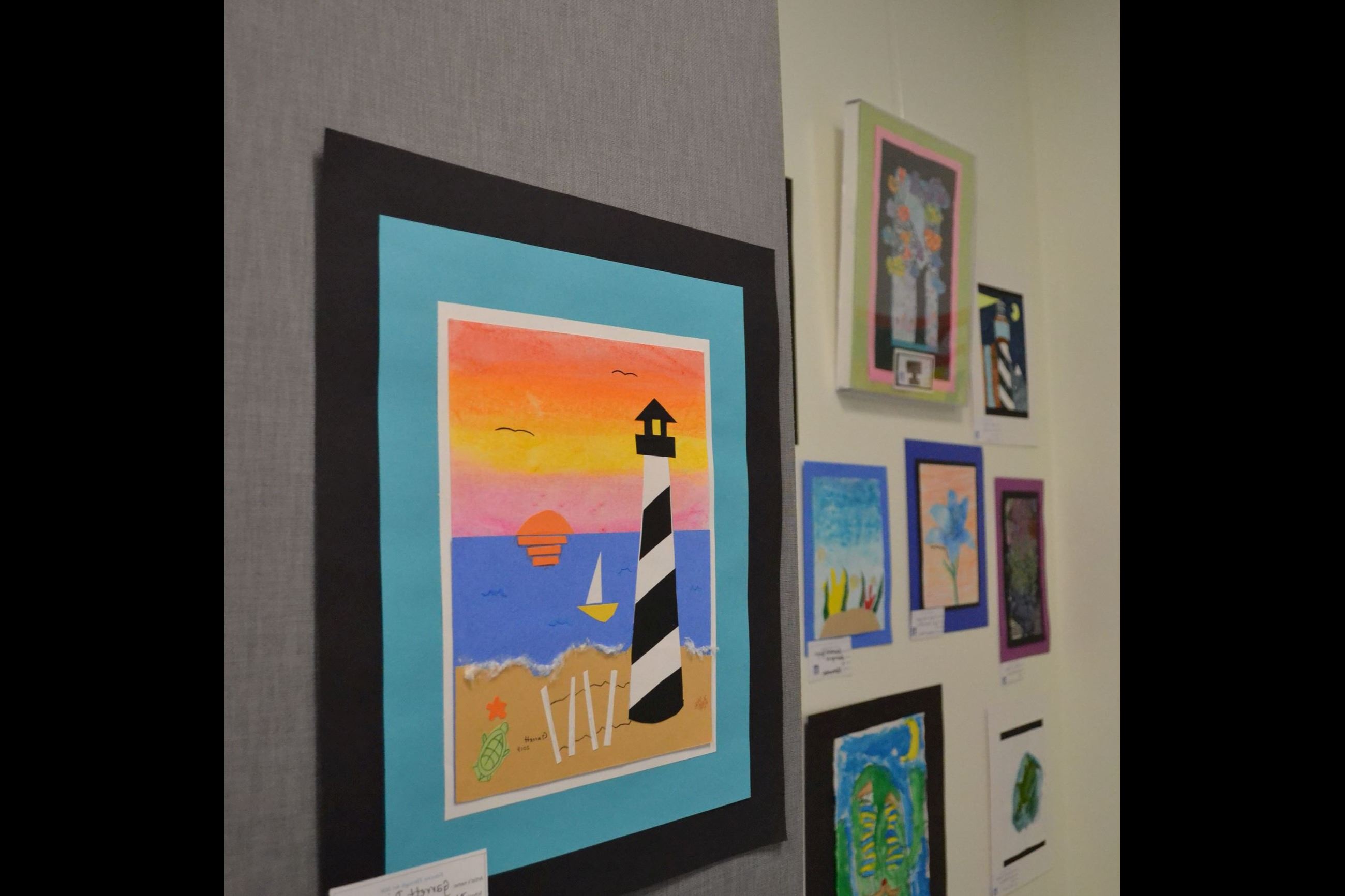 A colored drawing of a lighthouse on the beach with the ocean in the background. 
